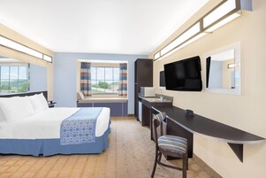Una habitación de hotel con cama, escritorio, silla, televisión y ventana con cortinas.