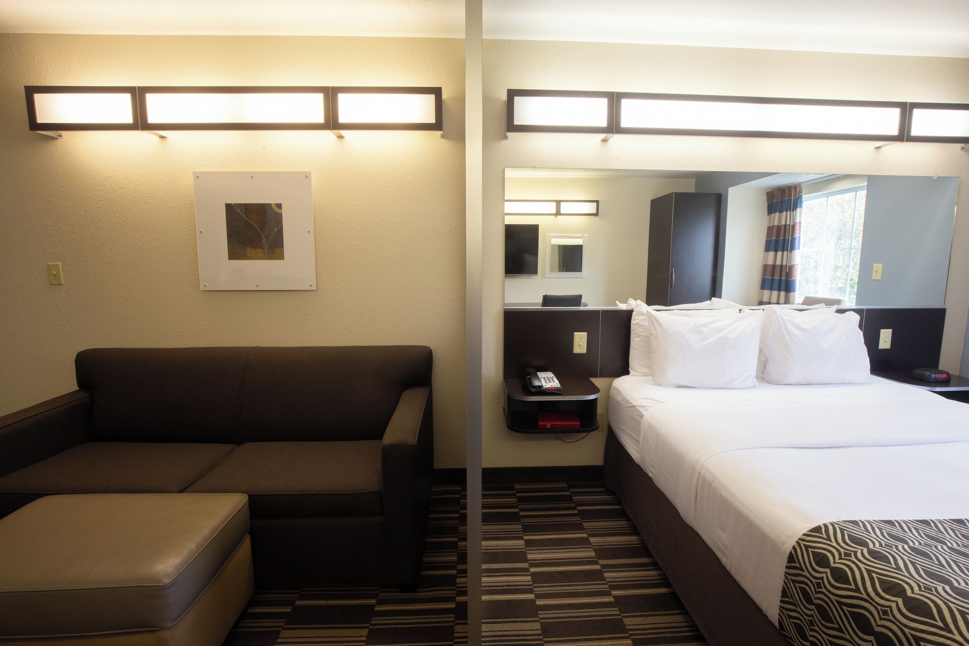 Una habitación de hotel con sofá, cama, mesita de noche y espejo.