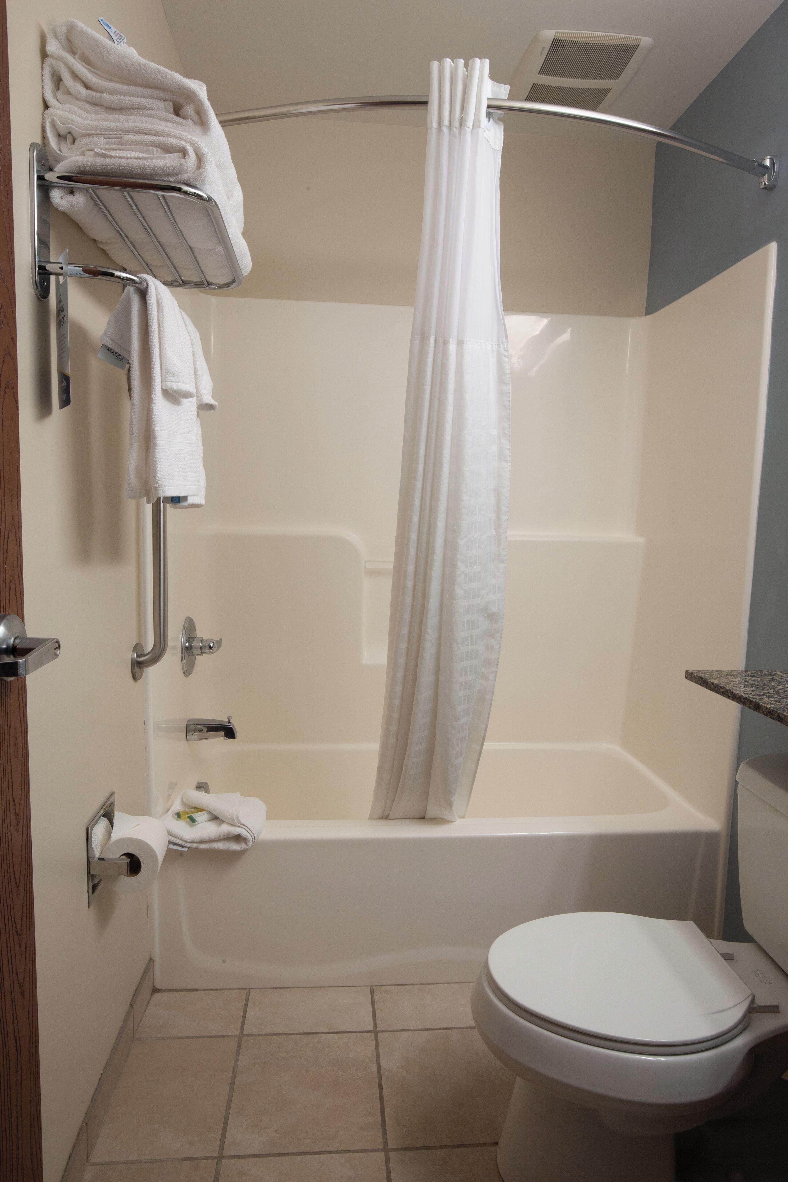 A bathroom with a bathtub, toilet, and a towel rack with folded towels.