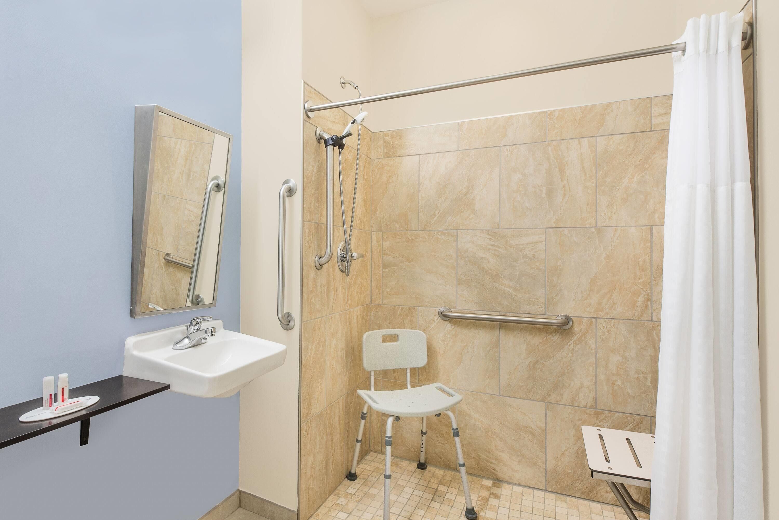 Un baño con ducha, lavamanos, espejo y silla de ruedas.