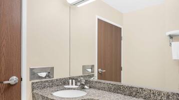 Un baño con lavamanos de encimera de granito, un espejo y una puerta de madera.
