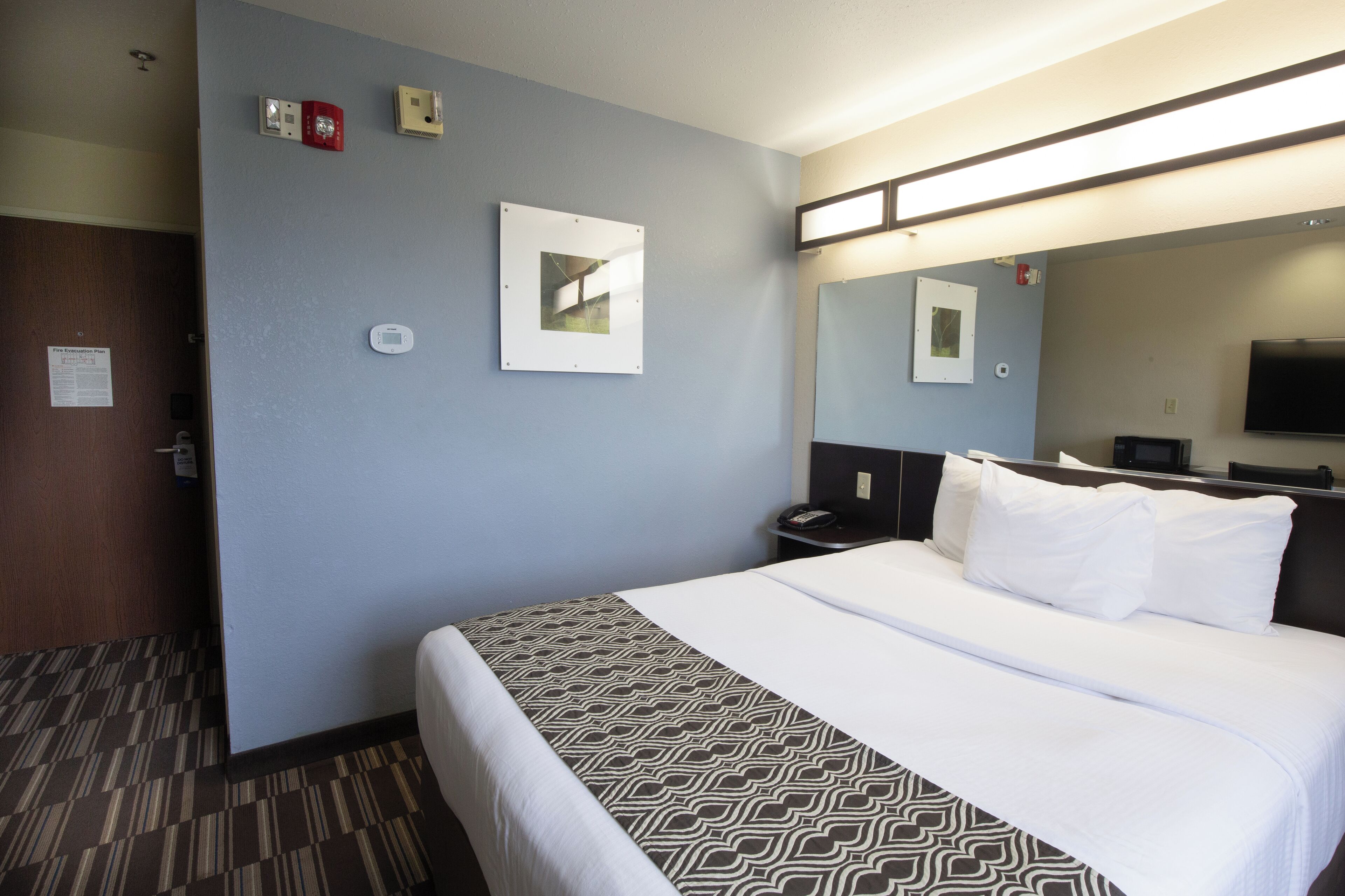 A hotel room with a bed, a bedside table, a mirror, and a wall-mounted TV.