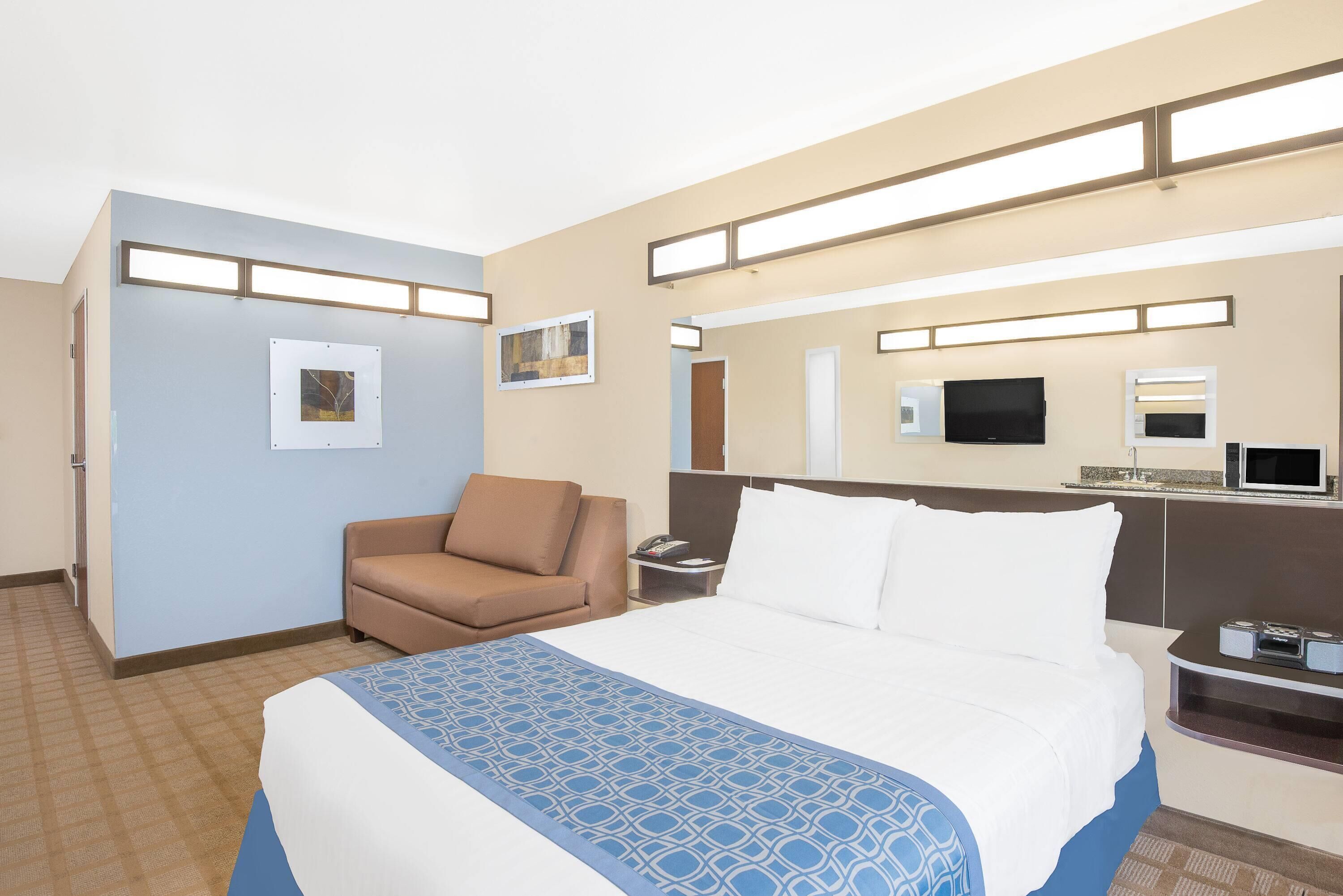 Une chambre d’hôtel avec un grand lit, un fauteuil brun, un bureau avec un téléviseur à écran plat et un four à micro-ondes.