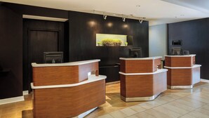 A reception area with wooden reception desks, a dark wall with a recessed light, and a small plant display. - Courtyard By Marriott Houston Medical Center Reliant Park (Houston)