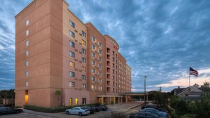 A multi-story hotel with a flat facade, multiple windows, and a parking lot with several cars. - Courtyard By Marriott Houston Medical Center Reliant Park (Houston)