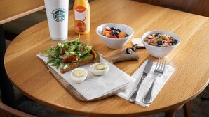 A wooden table with a breakfast setting including a cup, a bottle, a bowl of fruit, a plate with eggs, and cutlery. - Courtyard By Marriott Houston Medical Center Reliant Park (Houston)