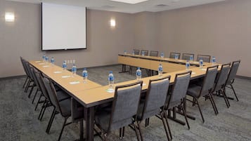 A conference room with a long table, chairs, water bottles, and a projector screen.