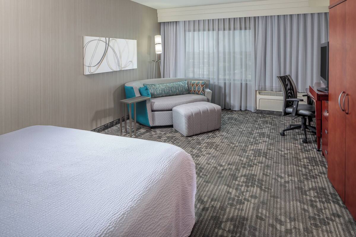 Une chambre d’hôtel avec un grand lit, un canapé, un bureau avec une chaise, une télévision et une fenêtre avec des rideaux.