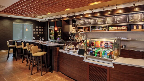 Een bar met een lange toonbank, barstoelen, een koelvitrine met drankjes en een menubord erboven.