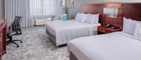 A hotel room with two beds, a desk, a chair, and a large window with curtains.