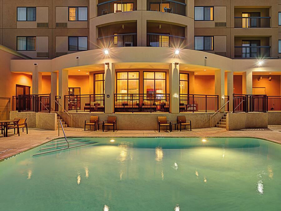 Zona de piscina de hotel con bar, asientos y vistas al exterior del edificio.