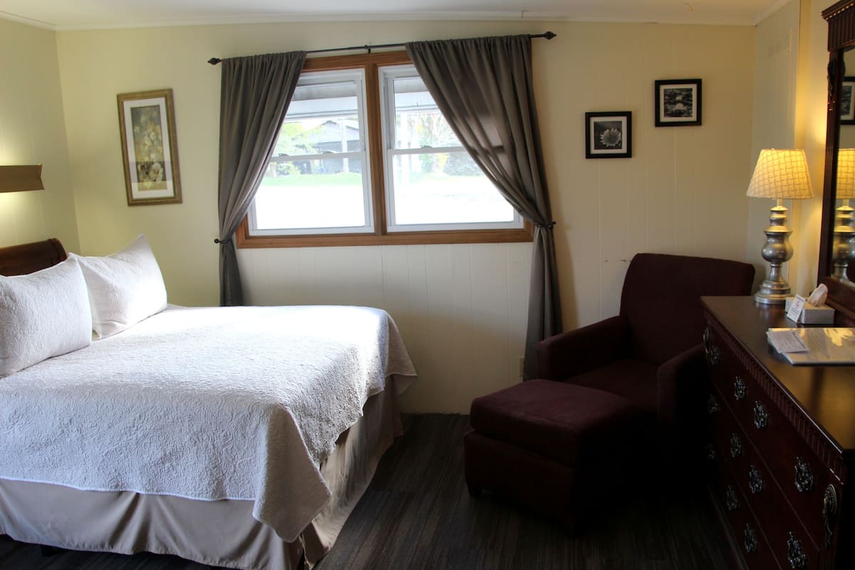 A hotel room with a bed, a chair, a dresser, and a window with curtains.