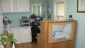 A reception area with a wooden desk, a computer, and framed pictures on the wall. - All Seasons Inn Corp (Oswego)