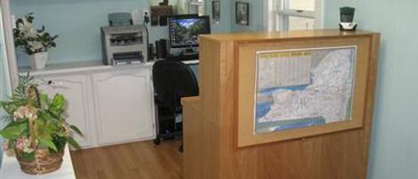 Un área de recepción con un escritorio de madera, una computadora y cuadros en la pared.
