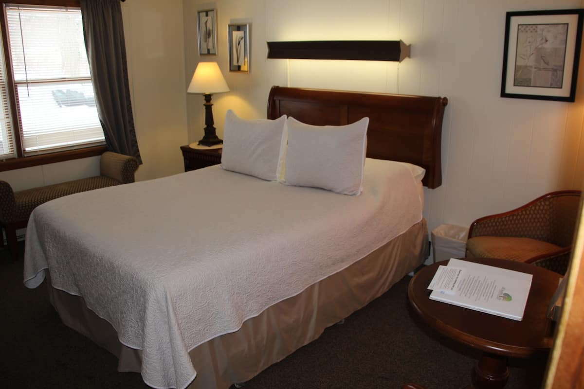 A neatly made bed with a wooden headboard, a bedside lamp, and a chair with a table beside it.