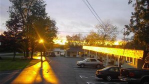 A parking lot with cars and a building with a covered area. - All Seasons Inn Corp (Oswego)