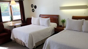 A hotel room with two beds, a sitting area with a chair, a small table, and a window with curtains.
