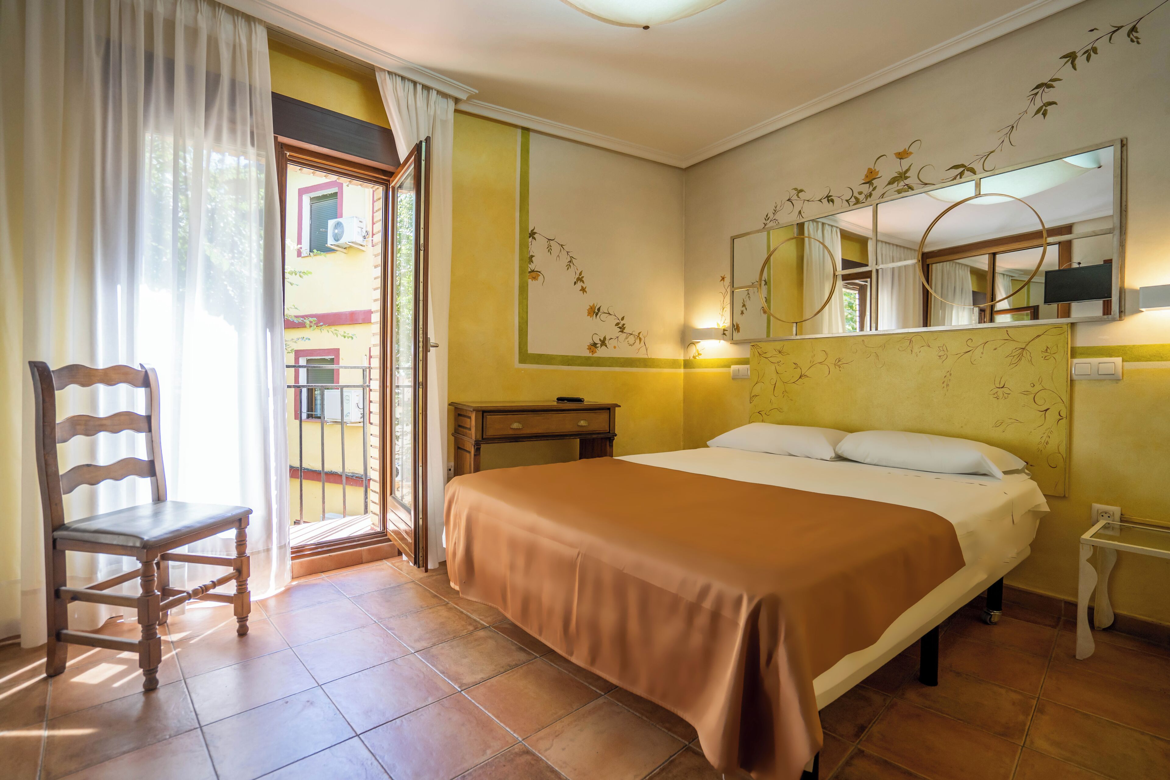 Habitación de hotel con una cama, una silla, una mesita de noche y una ventana con cortinas.