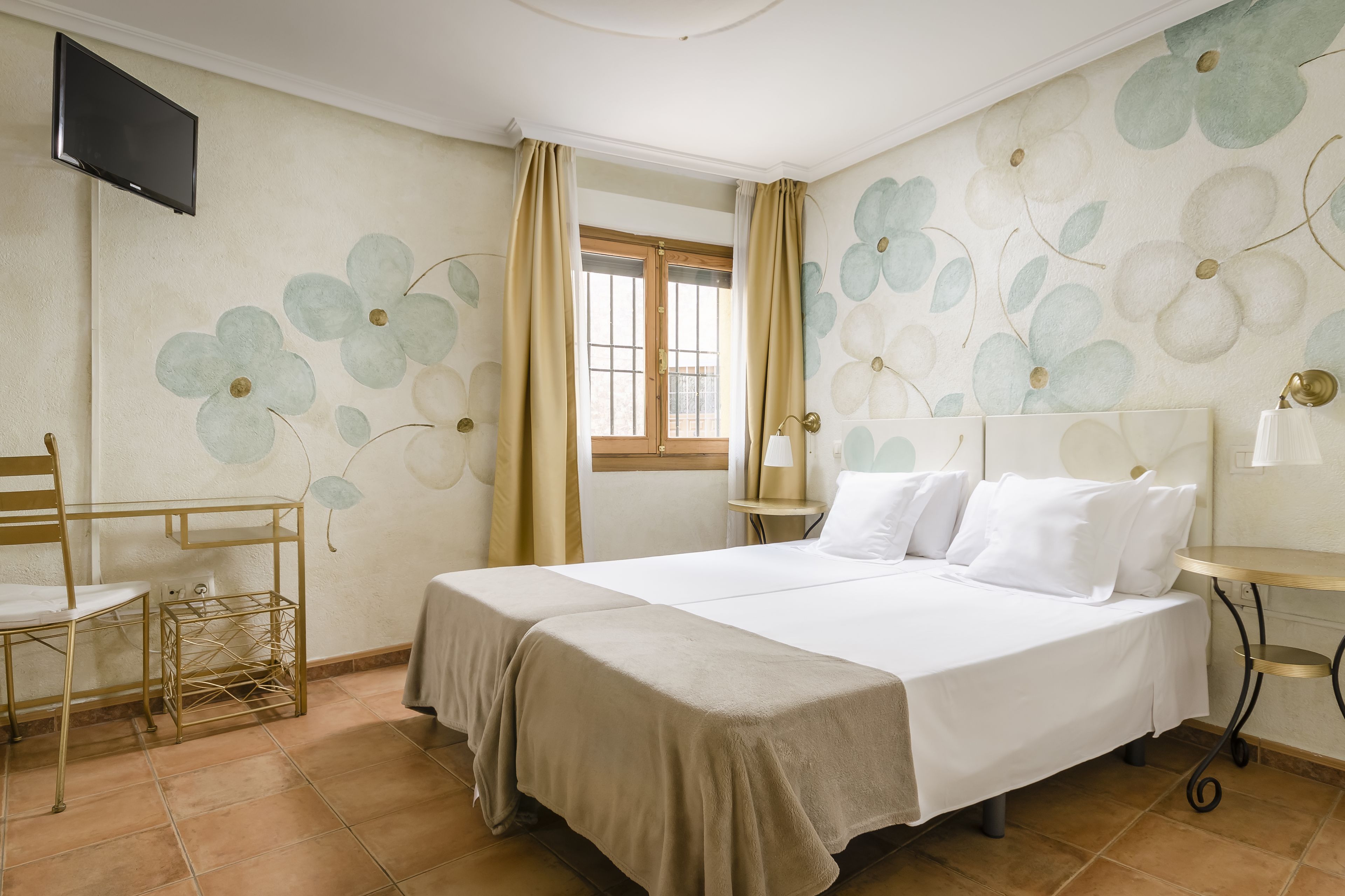 A hotel room with a bed, a desk, a chair, a TV, and a window with curtains.
