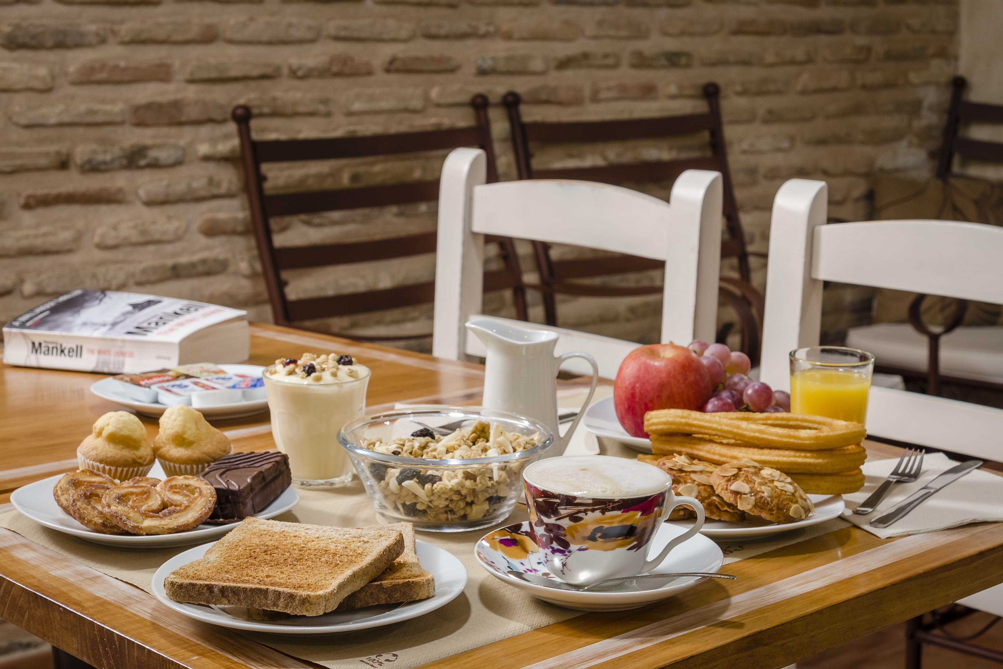 Una mesa de desayuno con diversos alimentos, una jarra, un vaso de jugo de naranja y un libro.