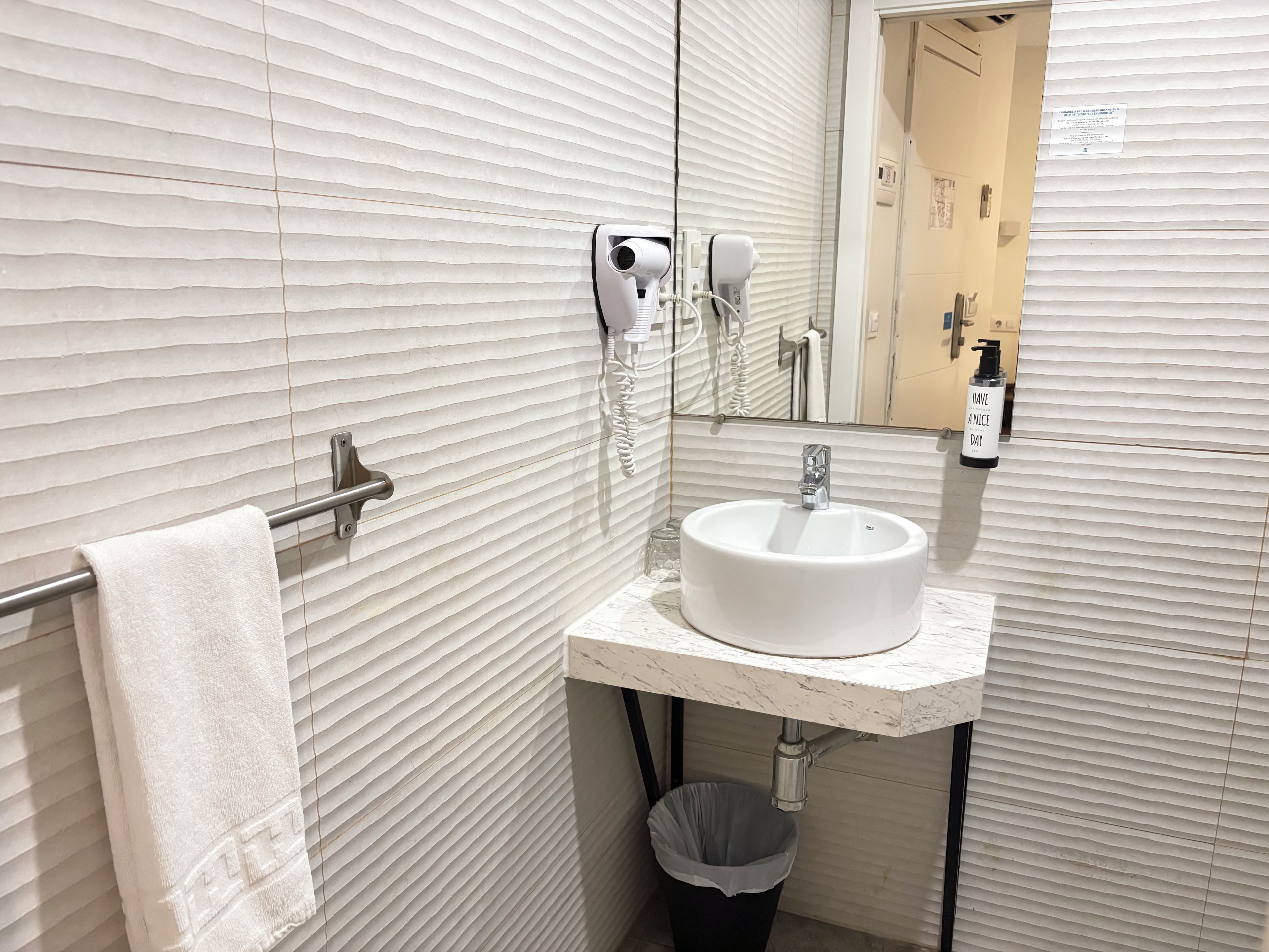 Un baño con toallero, lavamanos, espejo y cubo de basura.
