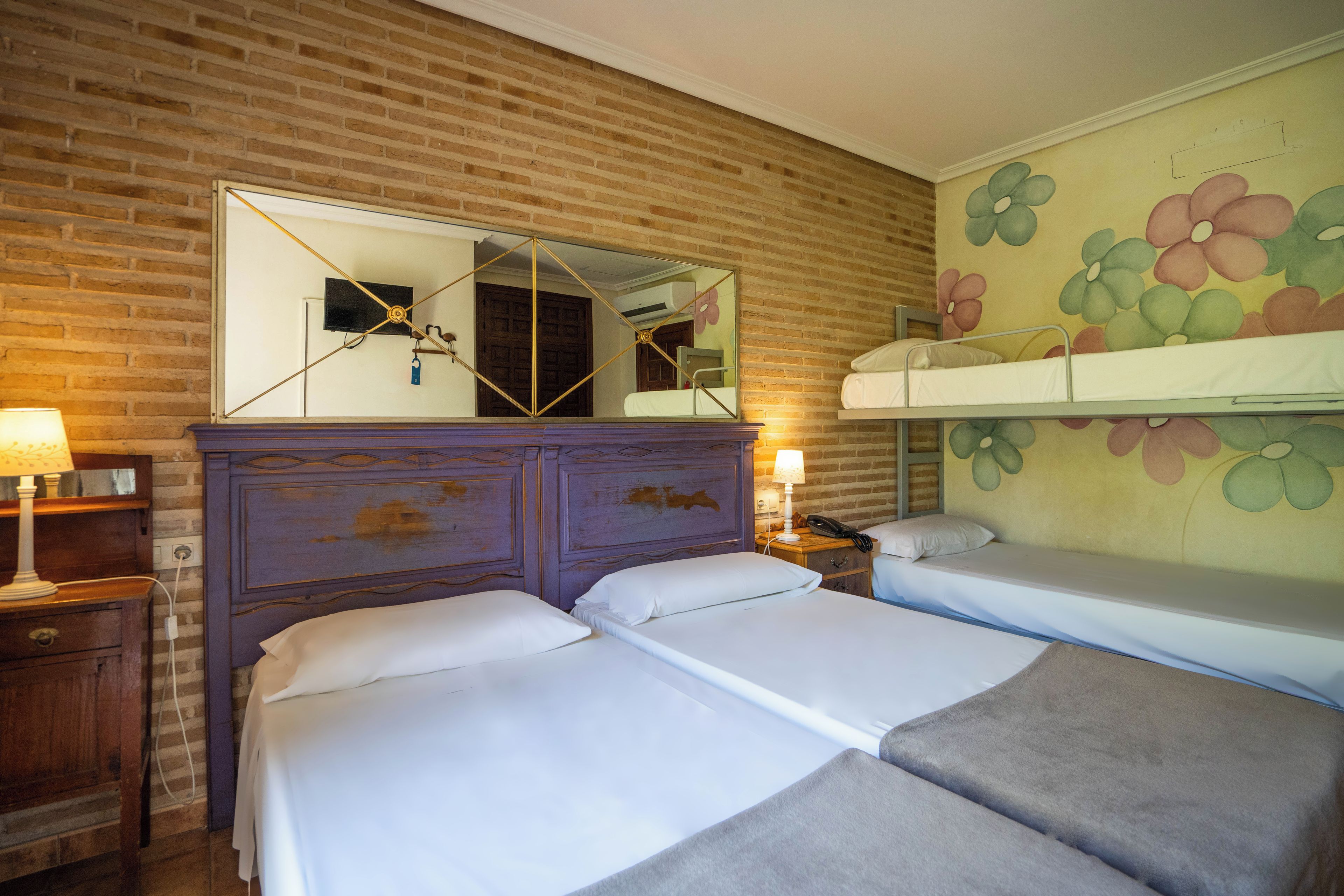 A room with two beds, a wooden dresser, a mirror, and a floral wall mural.