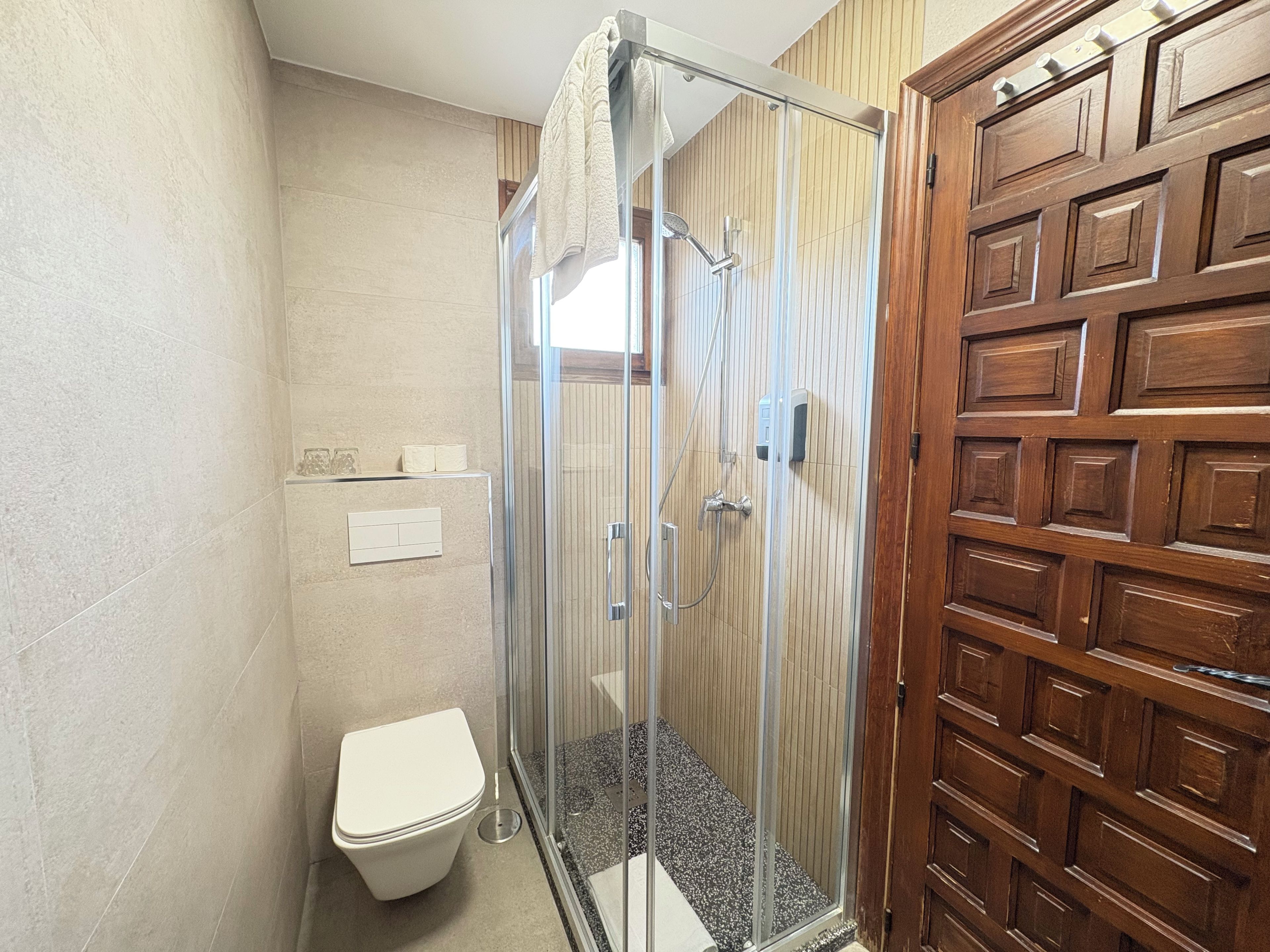 Une douche avec une porte en verre, des toilettes et une porte en bois ornée de panneaux décoratifs.