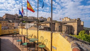 A terrace with outdoor seating and flags, overlooking historic buildings and a cityscape. - YIT Puerta Bisagra (Toledo)