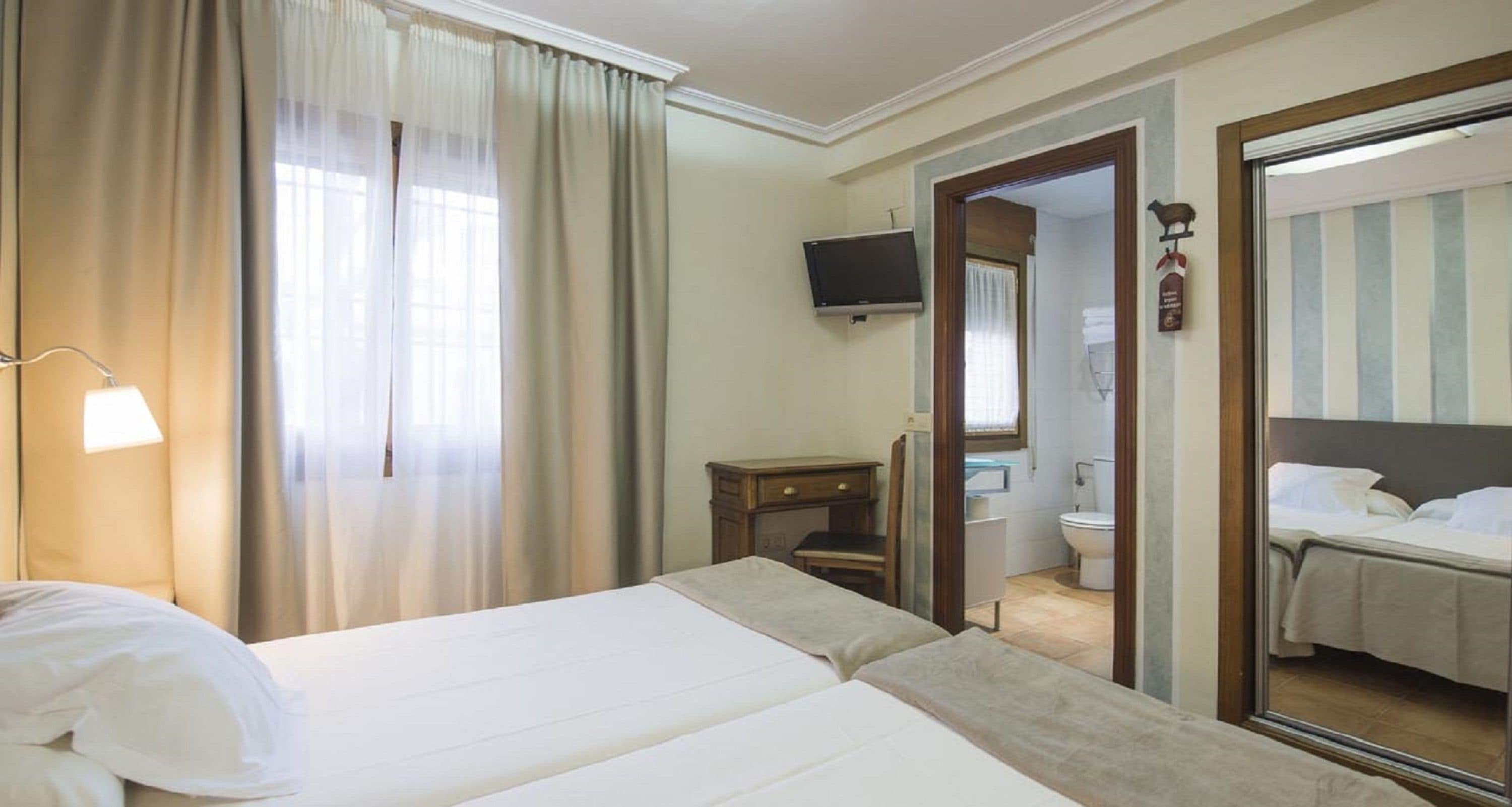 A hotel room with a bed, a desk, a television, and a bathroom visible through an open door.