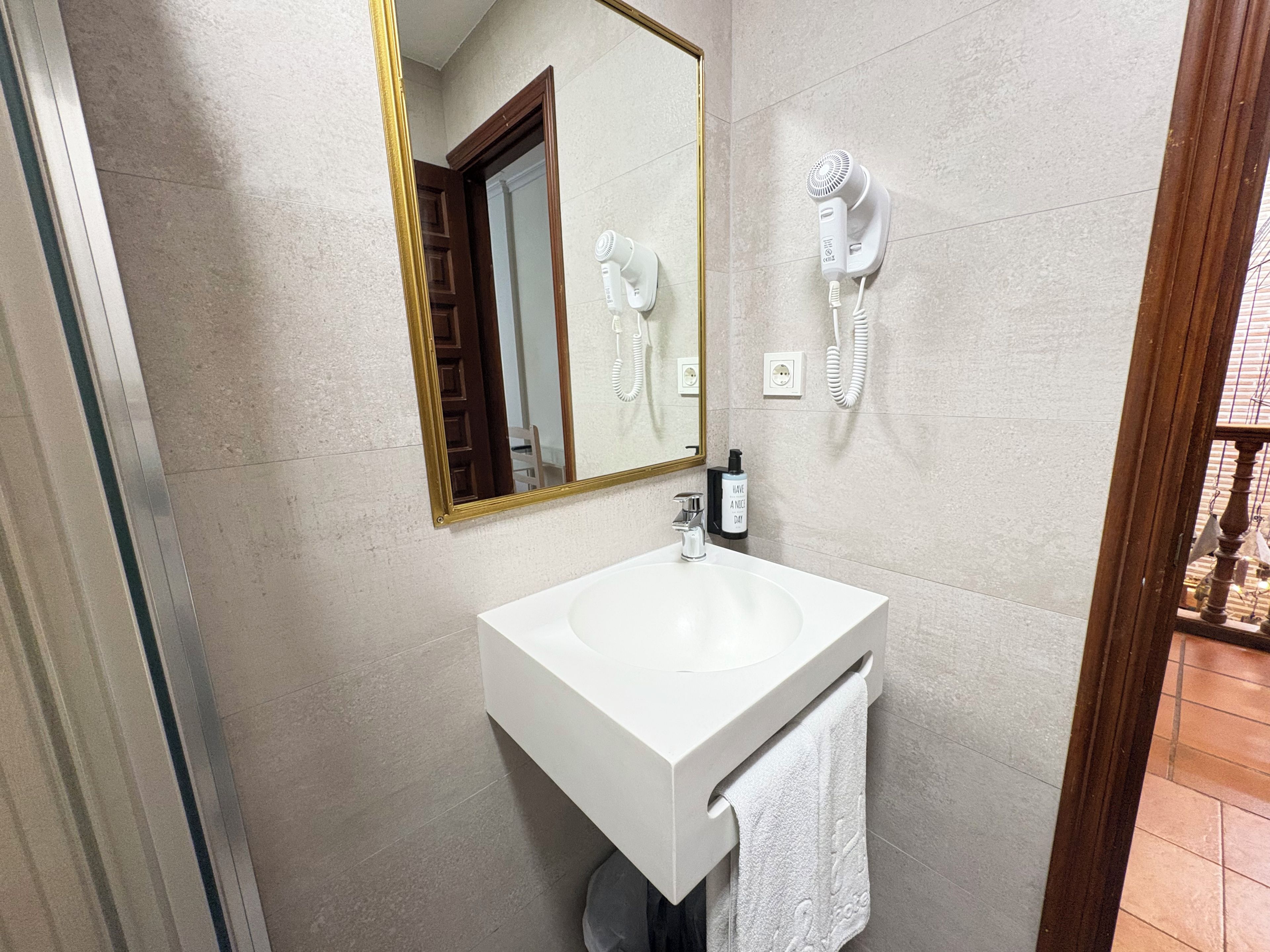 A bathroom with a white sink, a mirror with a gold frame, a hairdryer, and a towel hanging on the wall.