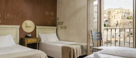 A hotel room with two beds, a wooden headboard, a nightstand, a hat on the wall, and a view of the city through a window.