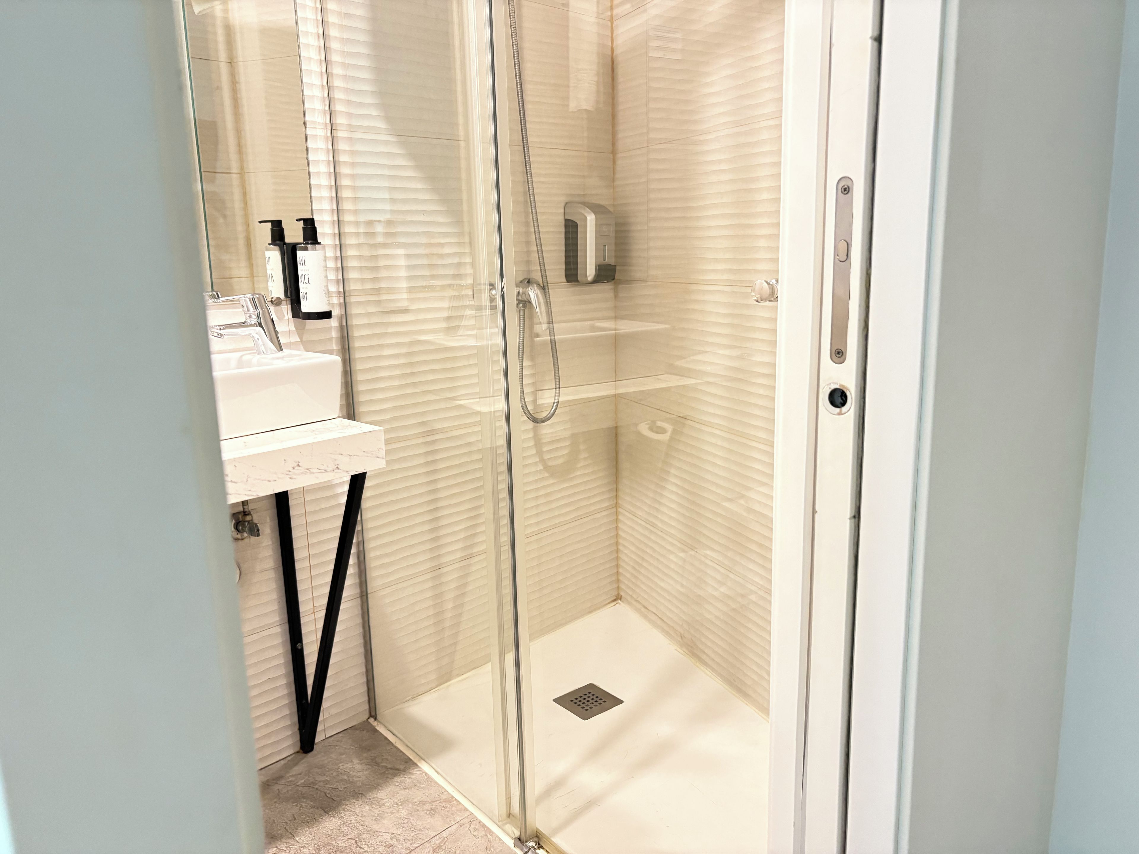 A modern bathroom with a glass-enclosed shower, a white sink, and a handheld showerhead.