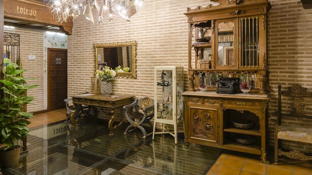 A room with a brick wall, a wooden cabinet with glass doors, a mirror, and a chandelier. - YIT Puerta Bisagra (Toledo)
