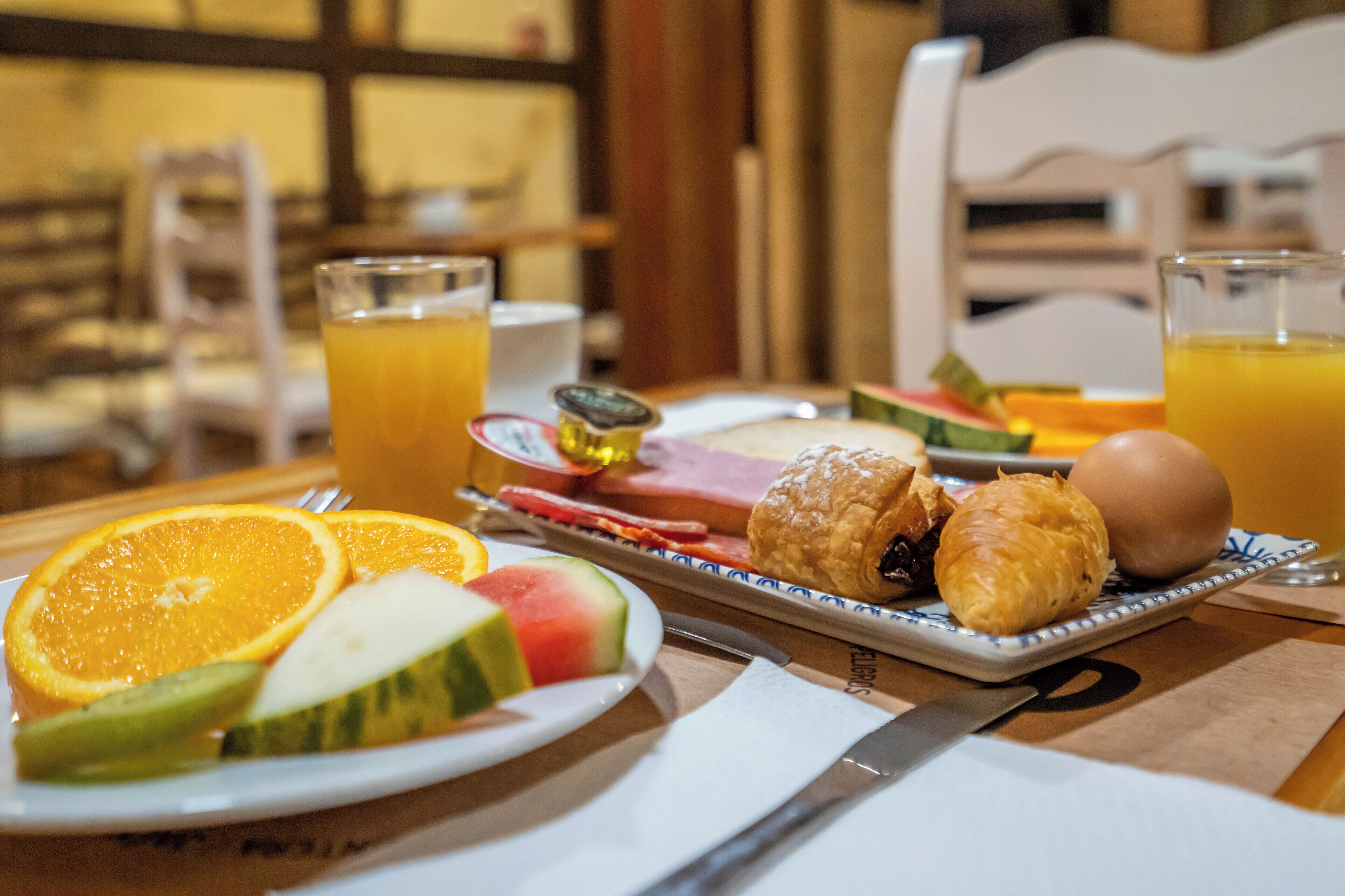 Desayuno con platos de fruta, croissants y un huevo duro, junto con vasos de jugo de naranja.