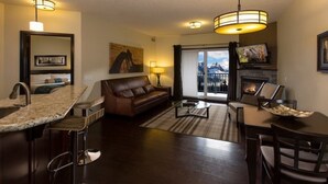 A modern living room with a fireplace, a sofa, a coffee table, and a dining area. - Grande Rockies Resort - Bellstar Hotels & Resorts (Canmore)