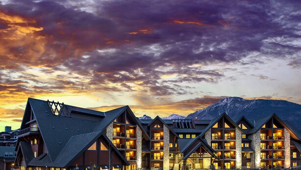 A hotel with multiple floors and balconies, set against a mountainous backdrop during sunset. - Grande Rockies Resort - Bellstar Hotels & Resorts (Canmore)