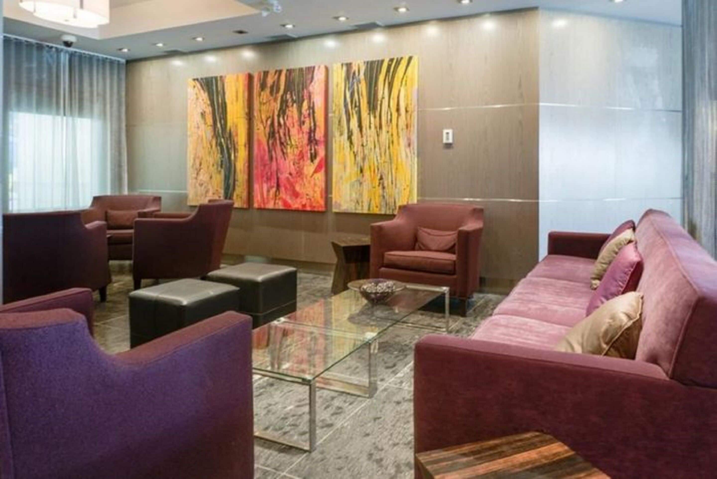 A modern lounge area with plush seating, a glass coffee table, and abstract wall art.