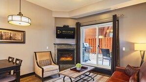 A living room with a fireplace, a dining table with chairs, a sofa, and a television mounted on the wall. - Grande Rockies Resort - Bellstar Hotels & Resorts (Canmore)