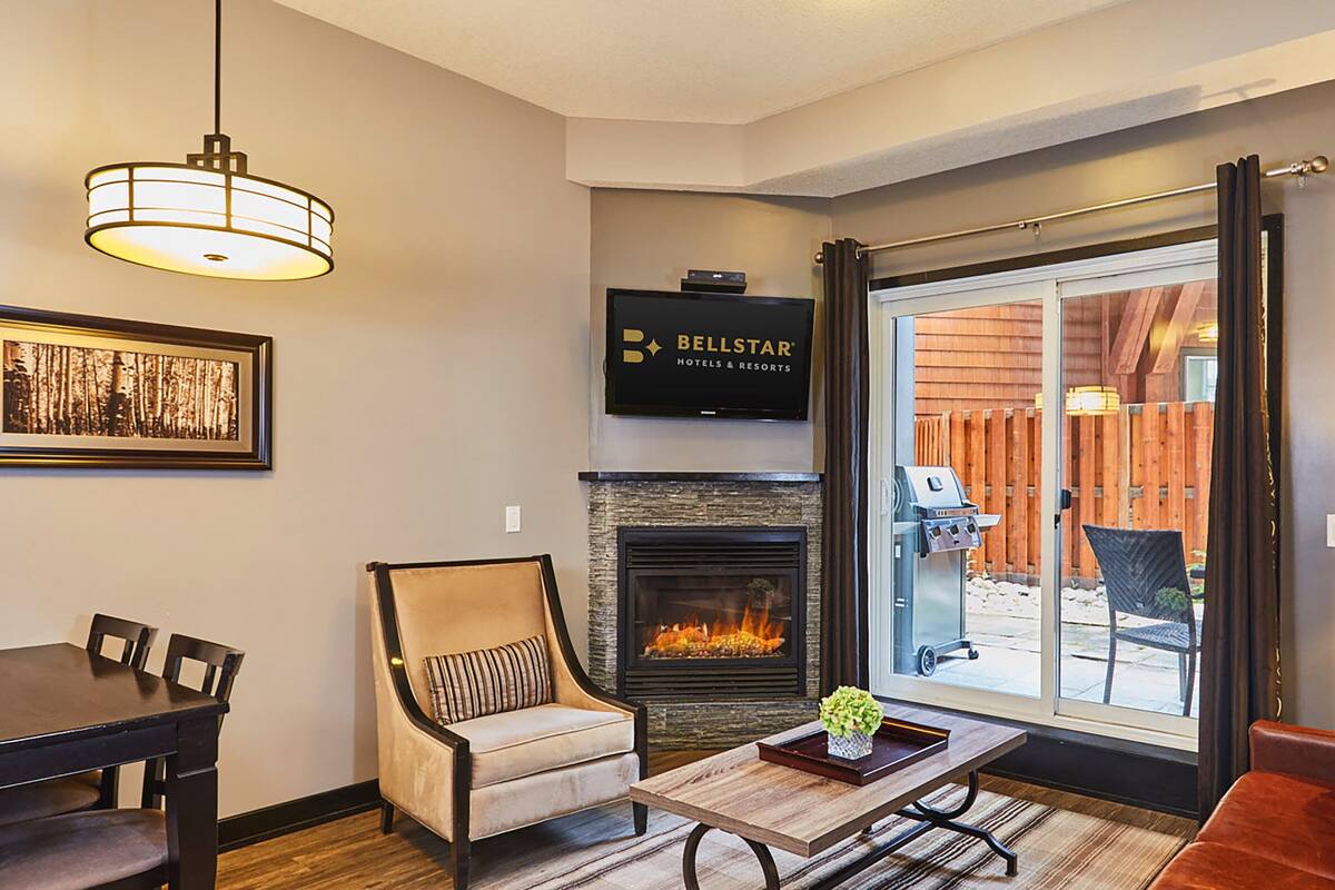 A living room with a fireplace, a dining table with chairs, a sofa, and a television mounted on the wall.