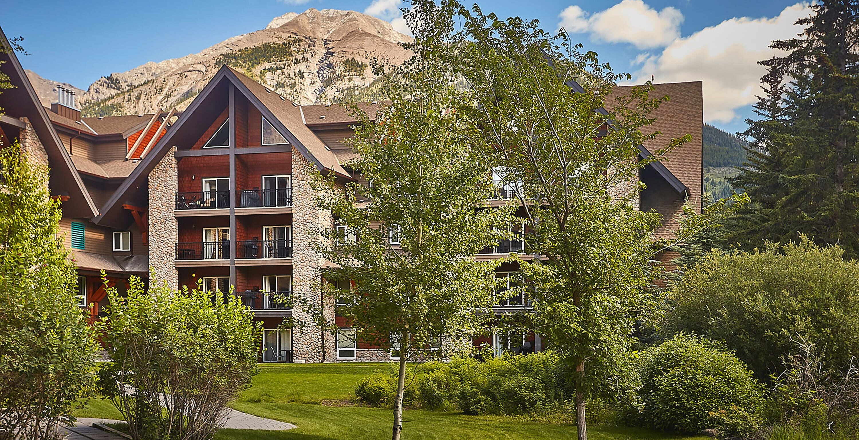 Ein mehrstöckiges Hotel mit Natursteinfassade, Balkonen und einem Berg im Hintergrund.