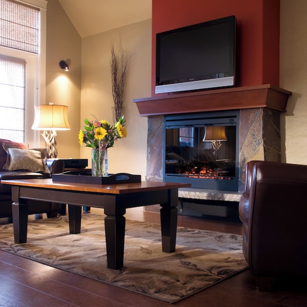 A living room with a fireplace, a television mounted above it, a coffee table, and a sofa.