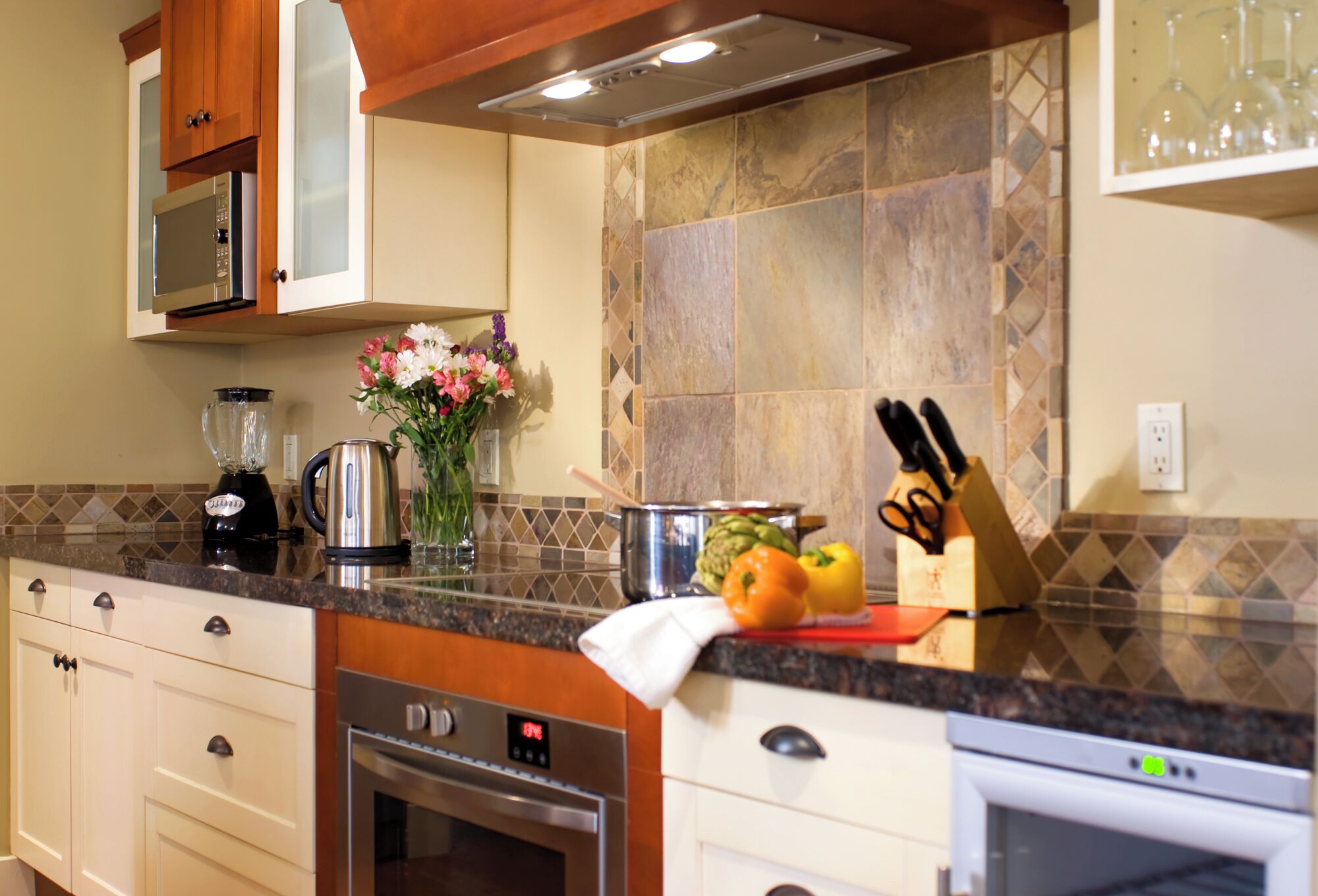 A kitchen with a microwave, oven, and coffee maker. There are vegetables on the counter and a knife block.