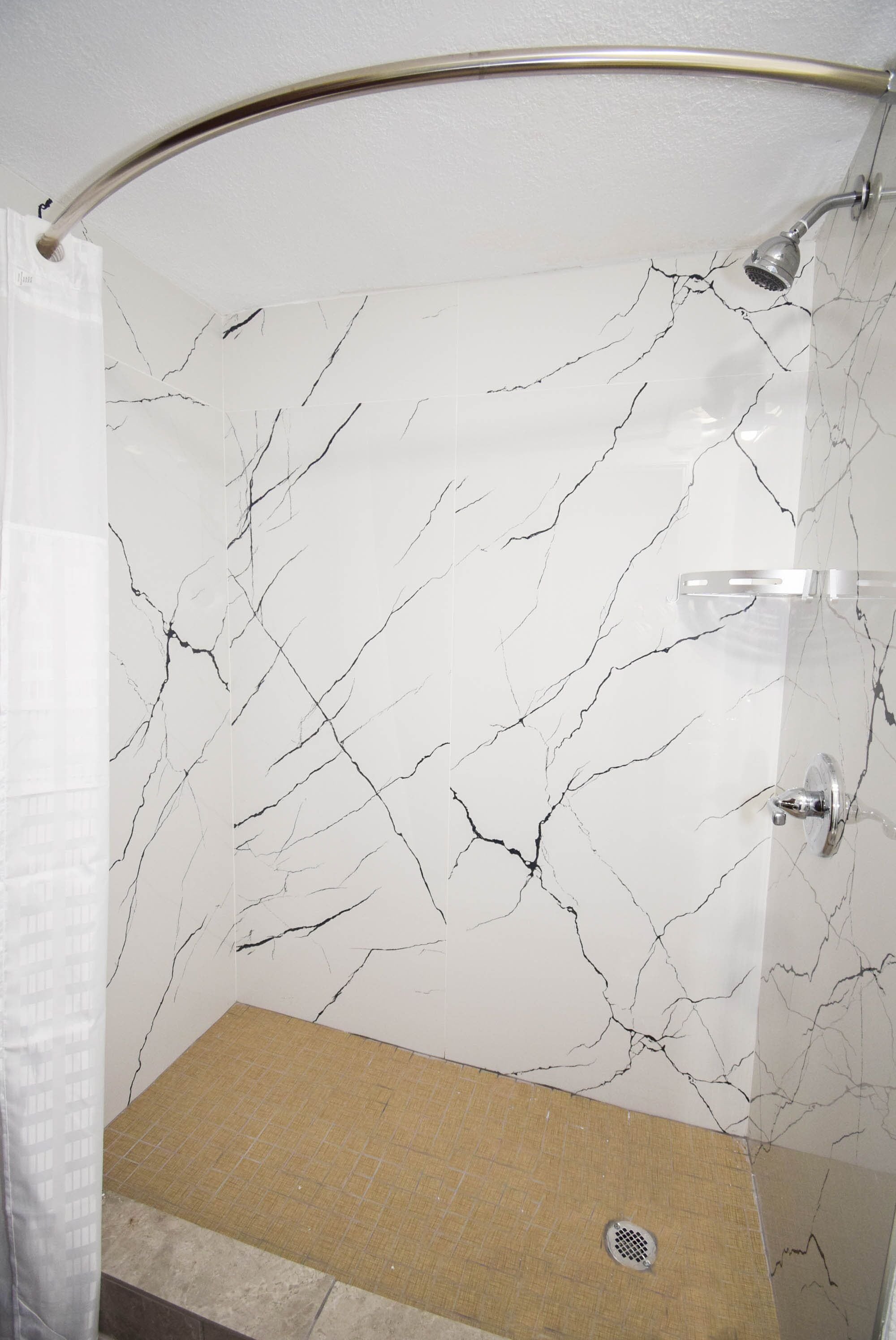 Un baño con pared de mármol blanco, zona de ducha y suelo color beige.