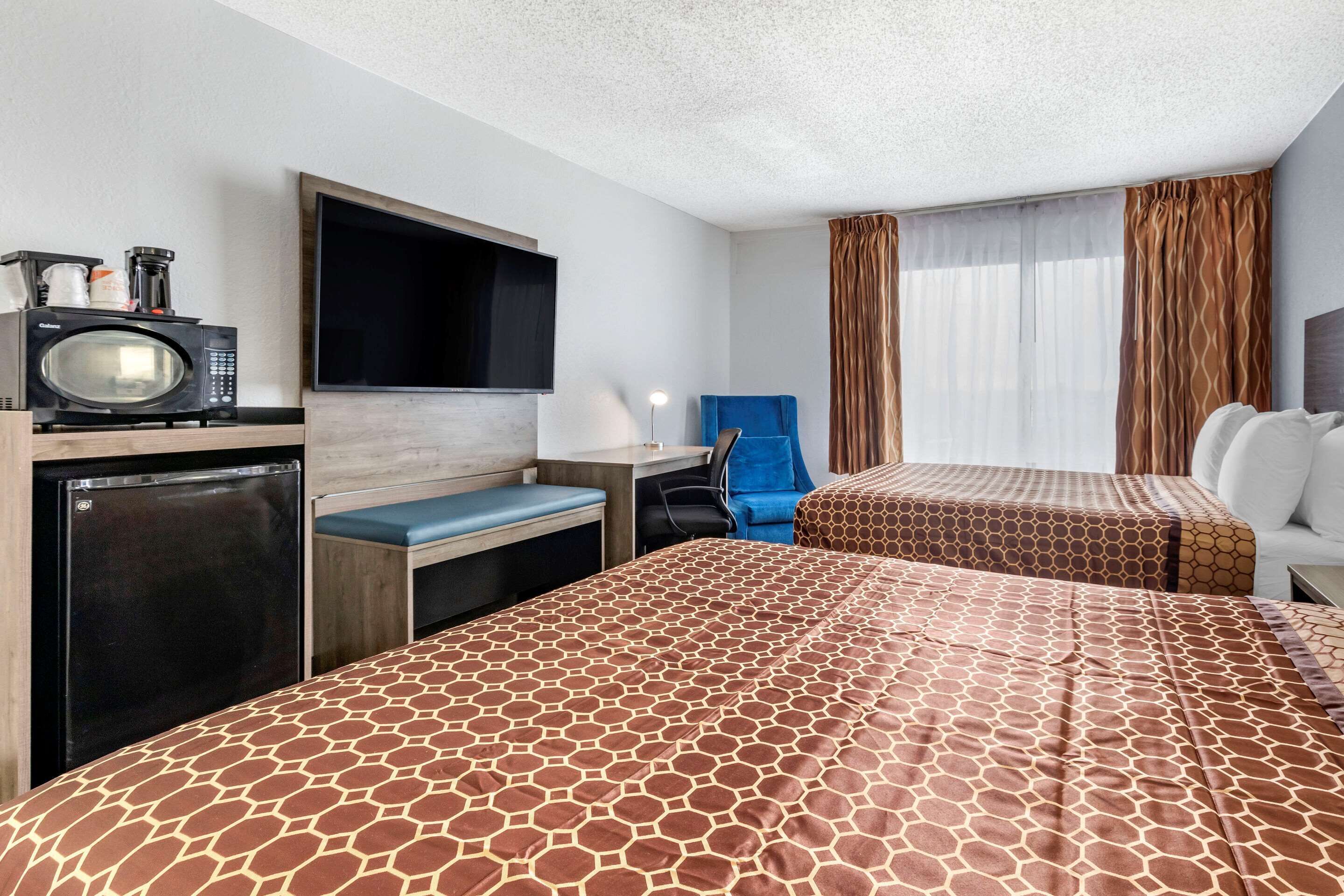 A hotel room with two beds, a TV, a microwave, a refrigerator, a desk, and a chair.