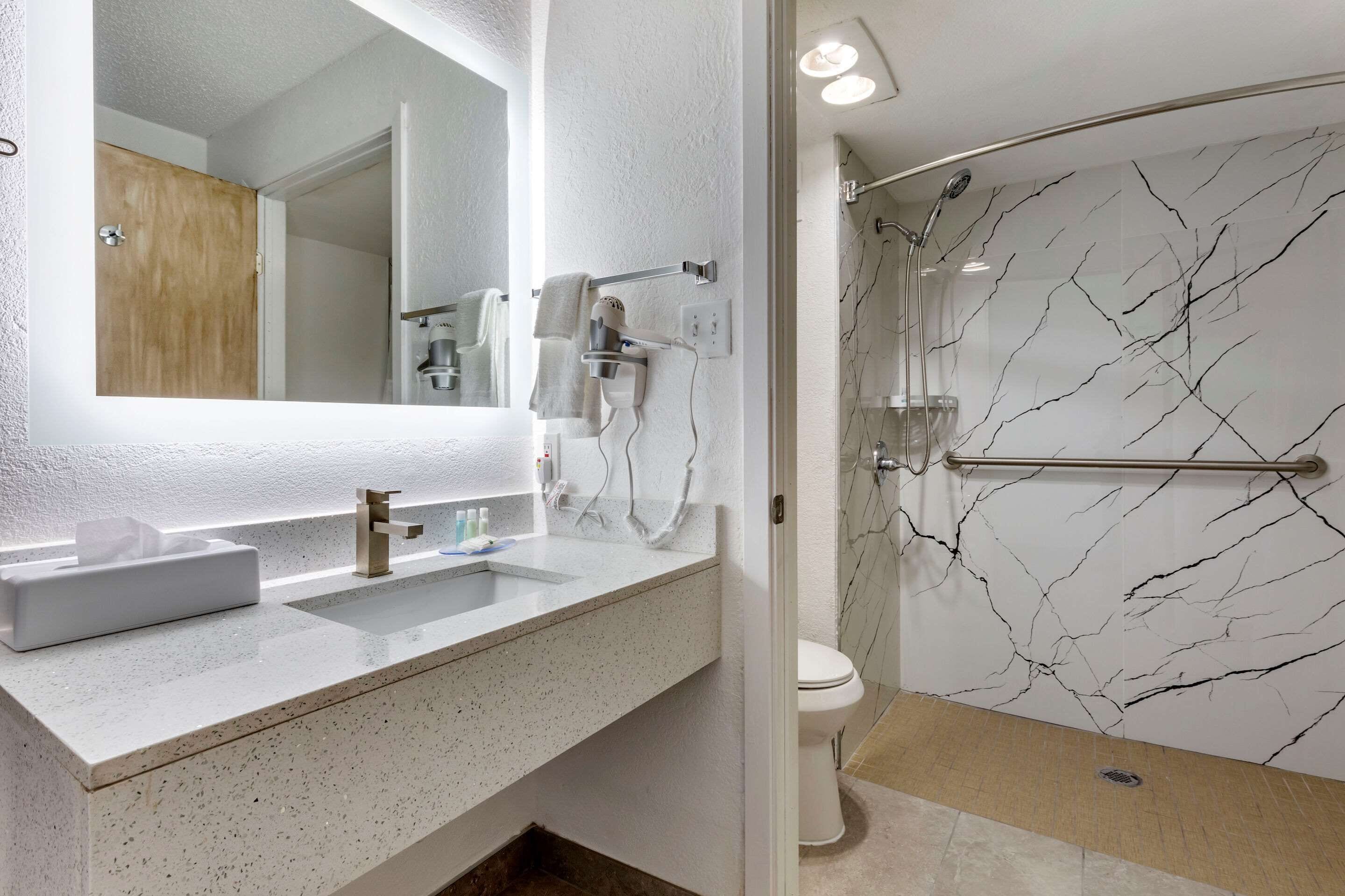 Une salle de bain avec un mur en marbre blanc, un lavabo avec un miroir et un espace douche.