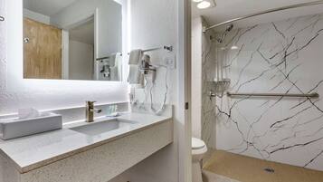 Une salle de bain avec un mur en marbre blanc, un lavabo avec un miroir et un espace douche.