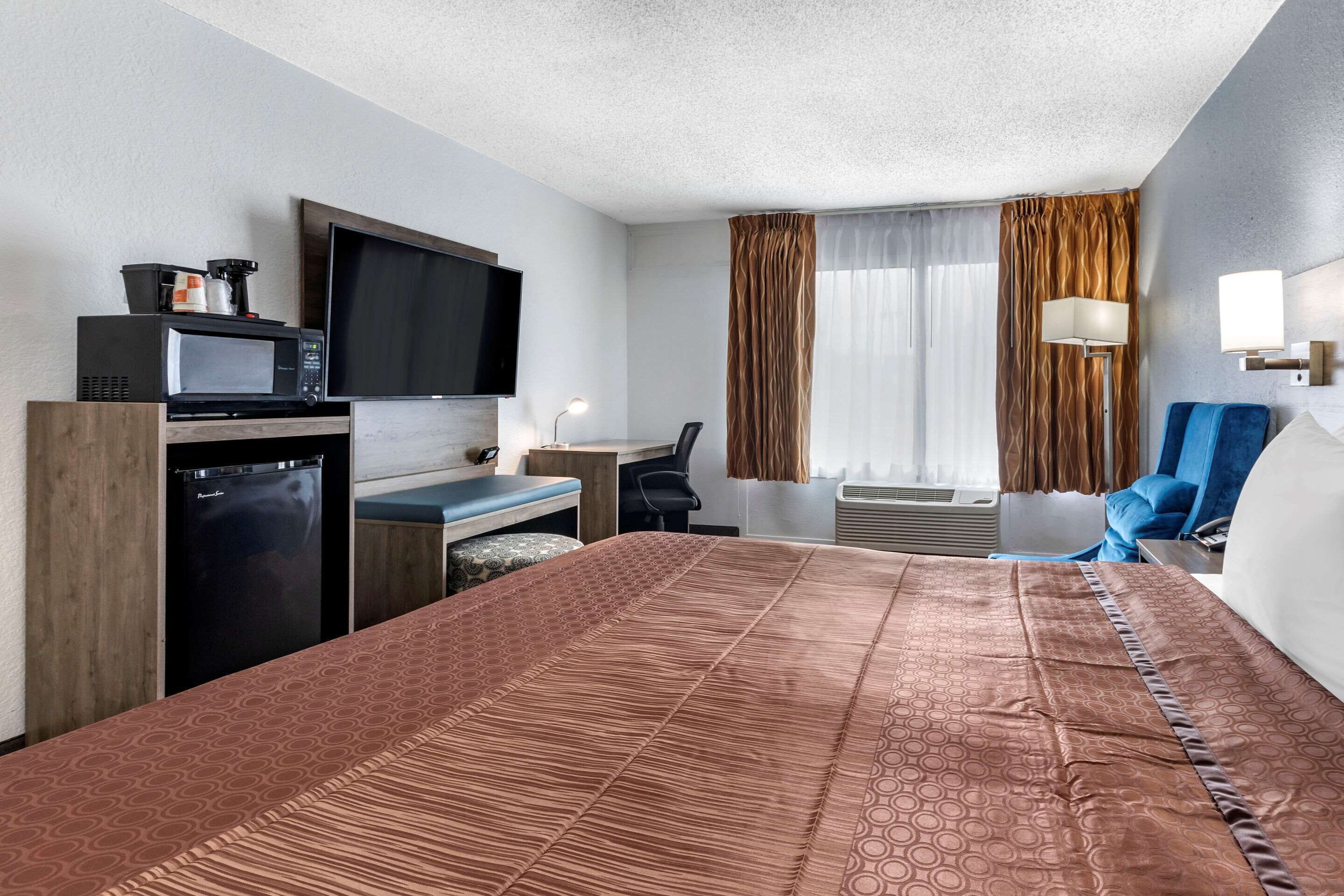 Ein Hotelzimmer mit einem Bett, einem Schreibtisch, einem Fernseher, einer Mikrowelle, einem Kühlschrank und einem Fenster mit Vorhängen.