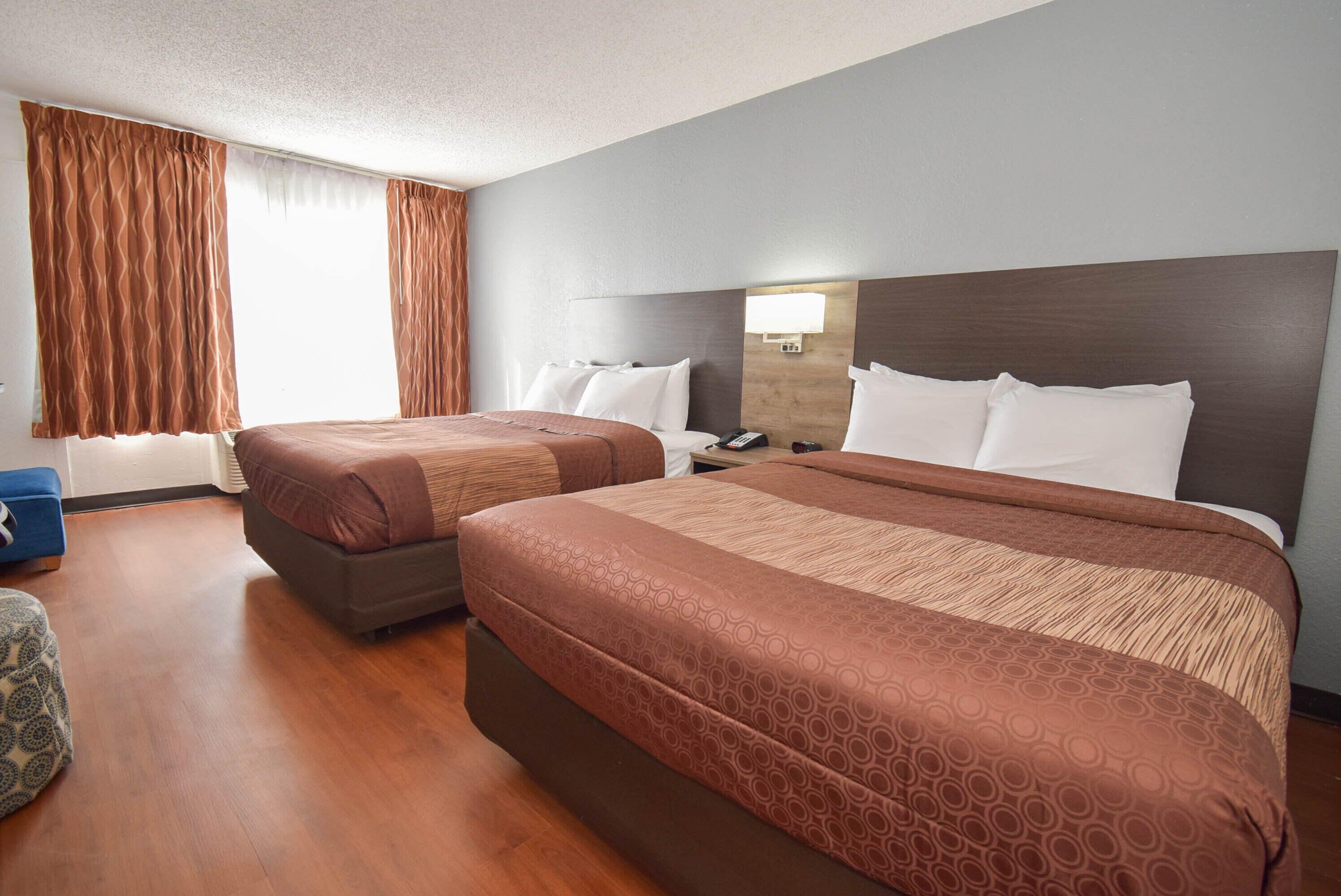 A hotel room with two beds, a nightstand, a lamp, and a blue chair.