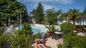 A pool area with lounge chairs and a small table, surrounded by greenery and a white fence. - Relais 500 de Vienne (Chonas-l'Amballan)