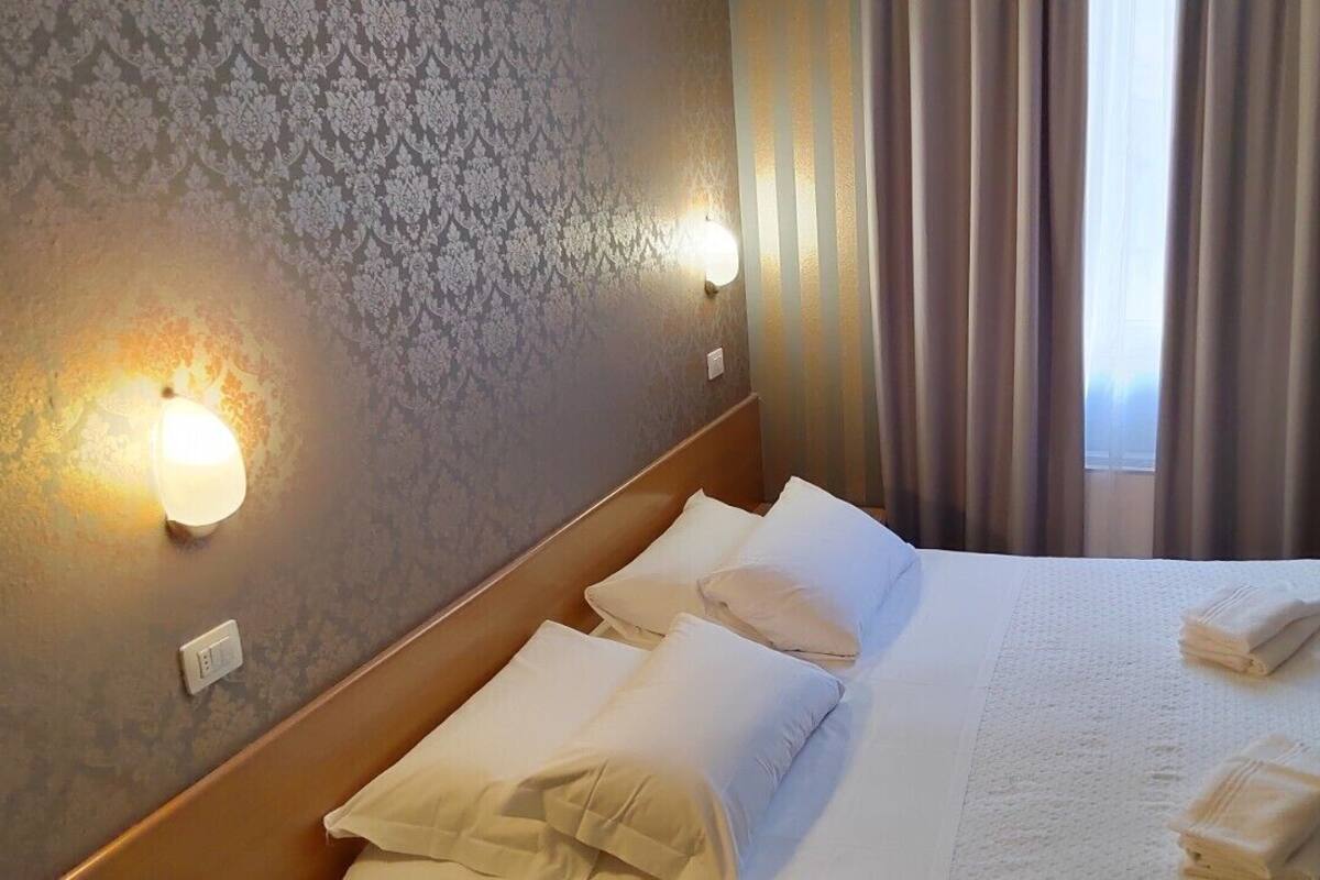 A hotel room with a neatly made bed, a wooden headboard, a wall-mounted TV, and a window with curtains.
